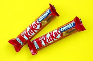 Kit Kat chocolate bars in red wrapping lies on bright yellow background. Kit kat created by Rowntree's of York in United Kingdom and is now produced globally by Nestle photo
