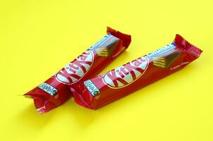 Kit Kat chocolate bars in red wrapping lies on bright yellow background. Kit kat created by Rowntree's of York in United Kingdom and is now produced globally by Nestle photo