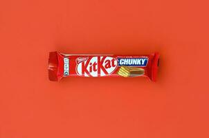 Kit Kat chocolate bar in red wrapping lies on bright red background. Kit kat created by Rowntree's of York in United Kingdom and is now produced globally by Nestle photo