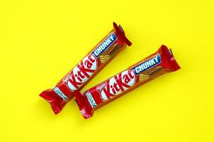 Kit Kat chocolate bars in red wrapping lies on bright yellow background. Kit kat created by Rowntree's of York in United Kingdom and is now produced globally by Nestle photo
