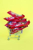 Kit Kat chocolate bars in small shopping cart on yellow background. Kit Kat is a famous brand of chocolates by Nestle company photo