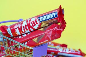 Kit Kat chocolate bars in small shopping cart on yellow background. Kit Kat is a famous brand of chocolates by Nestle company photo