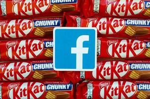 Facebook paper logo on many Kit Kat chocolate covered wafer bars in red wrapping. Advertising chocolate product in Facebook social network and world wide web photo