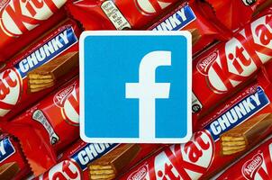 Facebook paper logo on many Kit Kat chocolate covered wafer bars in red wrapping. Advertising chocolate product in Facebook social network and world wide web photo