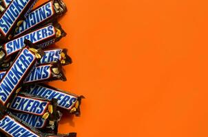Many Snickers chocolate bars lies on pastel orange paper. Snickers bars are produced by Mars Incorporated. Snickers was created by Franklin Clarence Mars in 1930 photo