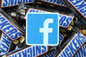 Facebook paper logo on many Snickers chocolate covered wafer bars in brown wrapping. Advertising chocolate product in Facebook social network and world wide web photo