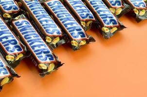 Many Snickers chocolate bars lies on pastel orange paper. Snickers bars are produced by Mars Incorporated. Snickers was created by Franklin Clarence Mars in 1930 photo