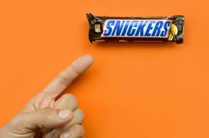 Hand holding a Snickers chocolate bar. Snickers bars are produced by Mars Incorporated. Snickers was created by Franklin Clarence Mars in 1930 photo