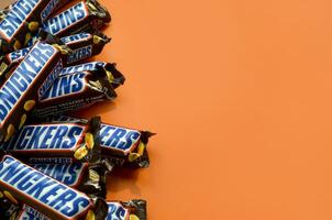 Many Snickers chocolate bars lies on pastel orange paper. Snickers bars are produced by Mars Incorporated. Snickers was created by Franklin Clarence Mars in 1930 photo