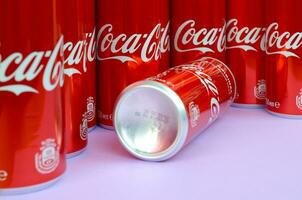 Coca-Cola logo printed on aluminium cans and placed on light lilac background. Most famous soda drink product company photo