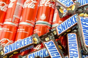 Snickers chocolate bars in brown wrapping lies on red Coca Cola tin cans close up. Famous drink and chocolate product photo