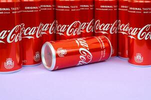 Coca-Cola logo printed on aluminium cans and placed on light lilac background. Most famous soda drink product company photo