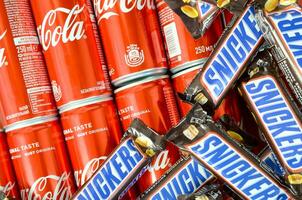 Snickers chocolate bars in brown wrapping lies on red Coca Cola tin cans close up. Famous drink and chocolate product photo