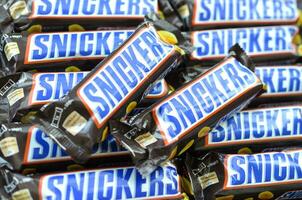 Many Snickers chocolate bars stacked close up. Snickers bars are produced by Mars Incorporated. Snickers was created by Franklin Clarence Mars in 1930 photo