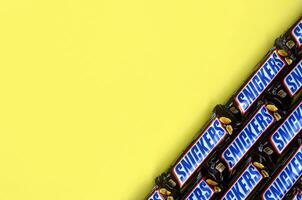 Many Snickers chocolate bars lies on pastel yellow paper. Snickers bars are produced by Mars Incorporated. Snickers was created by Franklin Clarence Mars in 1930 photo