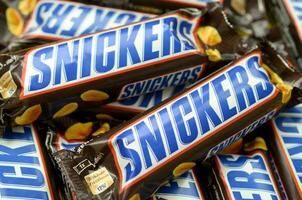 Many Snickers chocolate bars stacked close up. Snickers bars are produced by Mars Incorporated. Snickers was created by Franklin Clarence Mars in 1930 photo