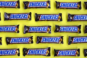 Many Snickers chocolate bars lies on pastel yellow paper. Snickers bars are produced by Mars Incorporated. Snickers was created by Franklin Clarence Mars in 1930 photo