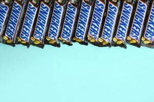 Many Snickers chocolate bars lies on pastel blue paper. Snickers bars are produced by Mars Incorporated. Snickers was created by Franklin Clarence Mars in 1930 photo