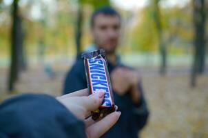 KHARKOV, UKRAINE - OCTOBER 8, 2019 Female hand passes the boy a Snickers chocolate bar in an autumn park. The manifestation of kindness photo