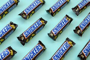 Many Snickers chocolate bars lies on pastel blue paper. Snickers bars are produced by Mars Incorporated. Snickers was created by Franklin Clarence Mars in 1930 photo