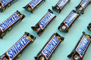 Many Snickers chocolate bars lies on pastel blue paper. Snickers bars are produced by Mars Incorporated. Snickers was created by Franklin Clarence Mars in 1930 photo