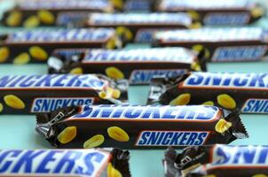 Many Snickers chocolate bars lies on pastel blue paper. Snickers bars are produced by Mars Incorporated. Snickers was created by Franklin Clarence Mars in 1930 photo