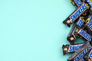 Many Snickers chocolate bars lies on pastel blue paper. Snickers bars are produced by Mars Incorporated. Snickers was created by Franklin Clarence Mars in 1930 photo