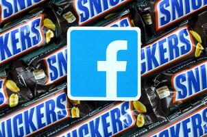 Facebook paper logo on many Snickers chocolate covered wafer bars in brown wrapping. Advertising chocolate product in Facebook social network and world wide web photo