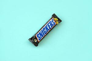 Many Snickers chocolate bars lies on pastel blue paper. Snickers bars are produced by Mars Incorporated. Snickers was created by Franklin Clarence Mars in 1930 photo