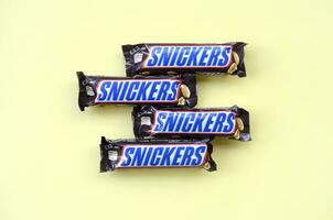 Many Snickers chocolate bars lies on pastel yellow paper. Snickers bars are produced by Mars Incorporated. Snickers was created by Franklin Clarence Mars in 1930 photo