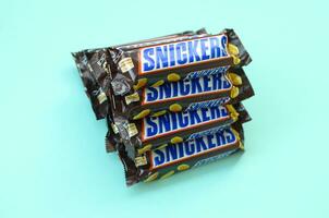 Many Snickers chocolate bars lies on pastel blue paper. Snickers bars are produced by Mars Incorporated. Snickers was created by Franklin Clarence Mars in 1930 photo