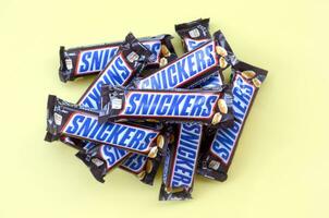 Many Snickers chocolate bars lies on pastel yellow paper. Snickers bars are produced by Mars Incorporated. Snickers was created by Franklin Clarence Mars in 1930 photo
