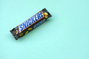 Many Snickers chocolate bars lies on pastel blue paper. Snickers bars are produced by Mars Incorporated. Snickers was created by Franklin Clarence Mars in 1930 photo