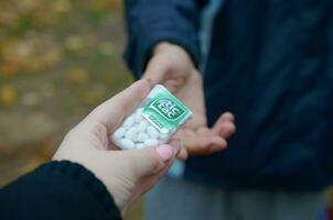 KHARKOV, UKRAINE - OCTOBER 26, 2019 Young man takes tic tac package to girl in autumn park. Tic tac is popular due its minty fresh taste by Ferrero photo