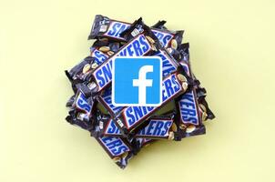 Facebook paper logo on many Snickers chocolate covered wafer bars in brown wrapping. Advertising chocolate product in Facebook social network and world wide web photo