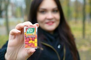KHARKOV, UKRAINE - OCTOBER 26, 2019 Young woman shows new Tic tac hard mints package in autumn park. Tic tac is popular due its minty fresh taste by Ferrero photo
