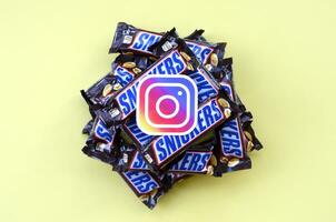 Instagram paper logo on many Snickers chocolate covered wafer bars in brown wrapping. Advertising chocolate product in Instagram social network and world wide web photo