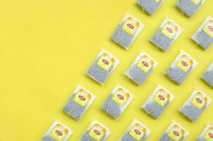 Flat lay of Lipton Yellow Label black tea bags on pastel yellow surface. Lipton is a world famous brand of tea photo