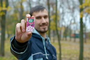 KHARKOV, UKRAINE - OCTOBER 26, 2019 Young man shows new Tic tac hard mints package in autumn park. Tic tac is popular due its minty fresh taste by Ferrero photo