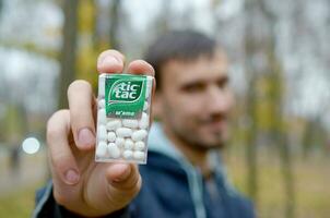 KHARKOV, UKRAINE - OCTOBER 26, 2019 Young man shows new Tic tac hard mints package in autumn park. Tic tac is popular due its minty fresh taste by Ferrero photo