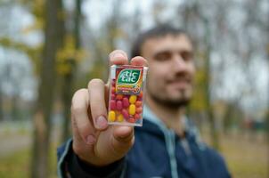 KHARKOV, UKRAINE - OCTOBER 26, 2019 Young man shows new Tic tac hard mints package in autumn park. Tic tac is popular due its minty fresh taste by Ferrero photo