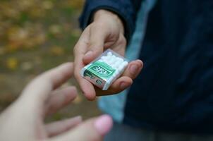 KHARKOV, UKRAINE - OCTOBER 26, 2019 Young man takes tic tac package to girl in autumn park. Tic tac is popular due its minty fresh taste by Ferrero photo