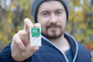 KHARKOV, UKRAINE - OCTOBER 26, 2019 Young man shows new Tic tac hard mints package in autumn park. Tic tac is popular due its minty fresh taste by Ferrero photo