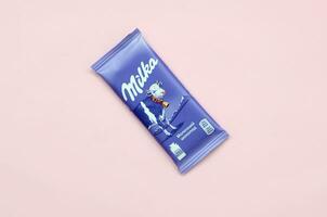 Milka chocolate tablet in classic violet wrapping on pastel pink background. Milka is brand of chocolate confection originated in Switzerland in 1901 photo