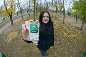 KHARKOV, UKRAINE - OCTOBER 26, 2019 Young woman shows new Tic tac hard mints package in autumn park. Tic tac is popular due its minty fresh taste by Ferrero photo