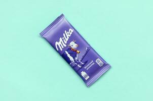 Milka chocolate tablet in classic violet wrapping on pastel blue background. Milka is brand of chocolate confection originated in Switzerland in 1901 photo