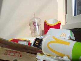 Used paper wrappings and disposable packs with McDonalds design and logo in pile on table. McDonalds recycle trash after usage photo