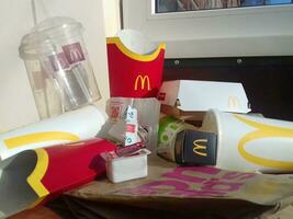 Used paper wrappings and disposable packs with McDonalds design and logo in pile on table. McDonalds recycle trash after usage photo