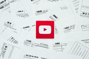 Printed Youtube logo on many tax form blanks lies on table close up. Help with tax problems using internet and information from social networks photo