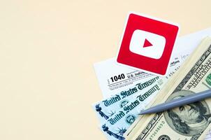 Youtube printed logo lies with 1040 Individual Income tax return form with Refund Check and hundred dollar bills on beige background. Help in tax period from social network concept photo